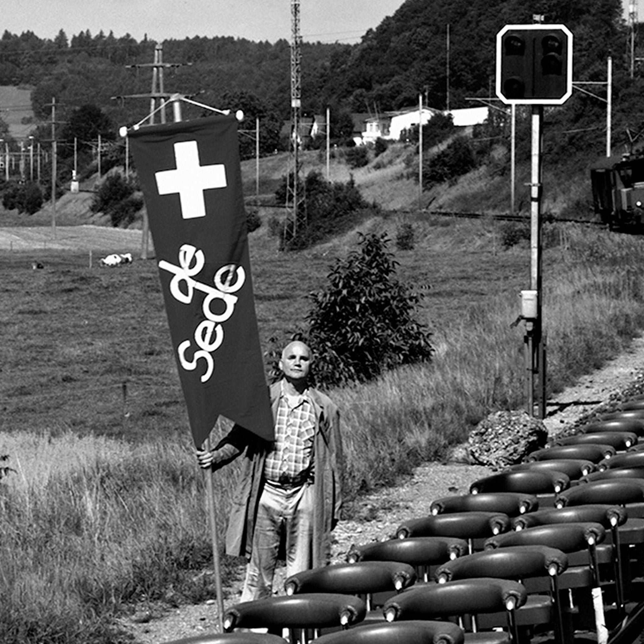 Eine Person hält ein Desede Switzerland Banner neben einer Reihe von Ledersesseln.