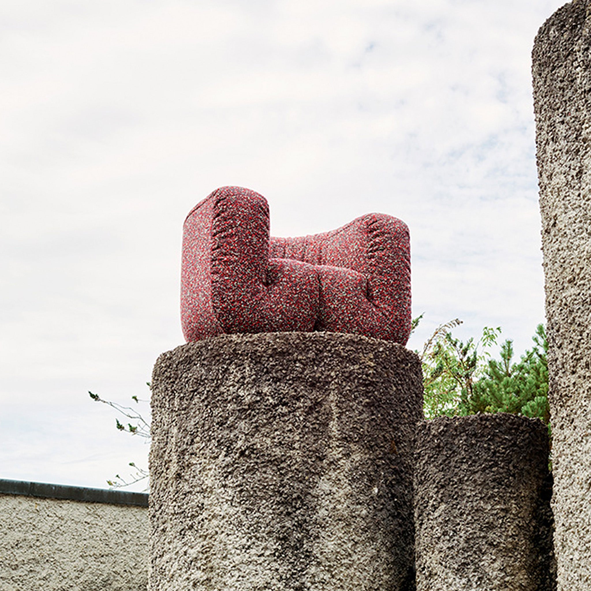 Roter Stoffsessel von Desede Switzerland auf Betonsockel, einzigartiges Designobjekt im Freien.